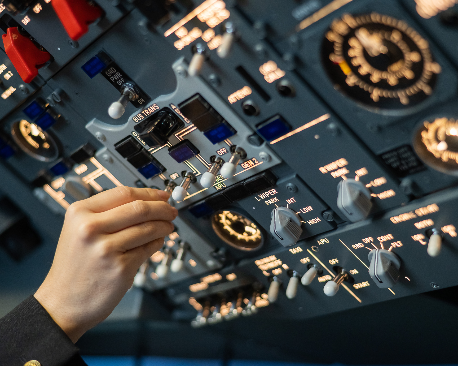 En hånd betjener en lille kontakt på et stort kontrolpanel med talrige målere og håndtag i cockpittet.