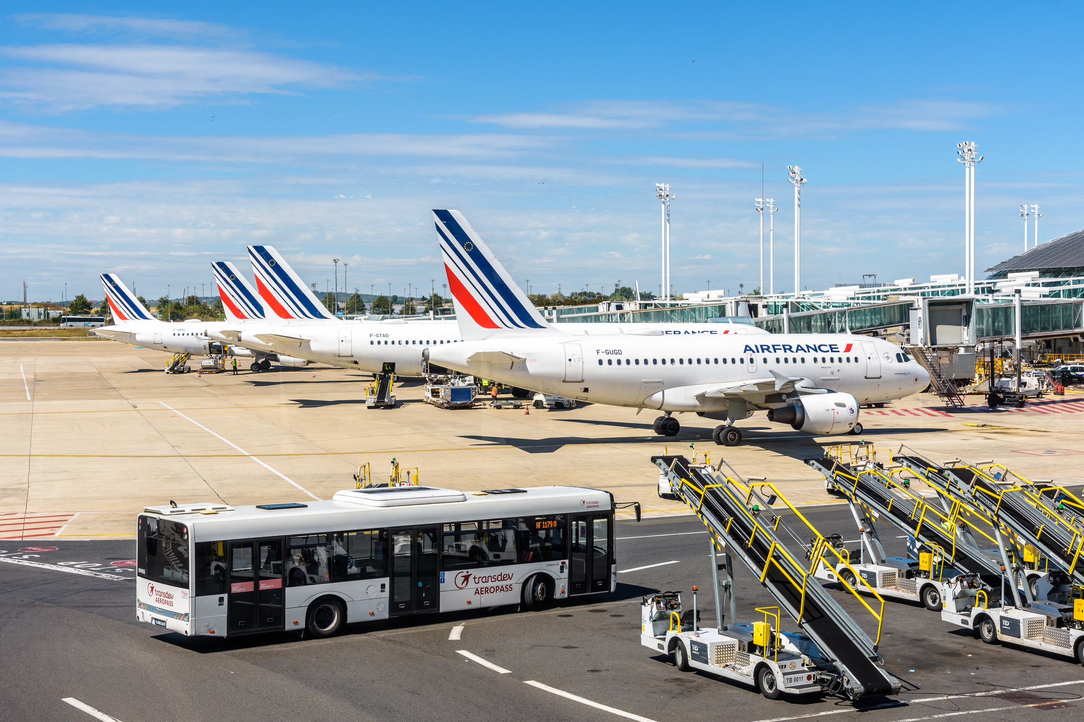 En række Air France-fly er parkeret side om side, i forgrunden kører en bus passagerer hen til flyene.