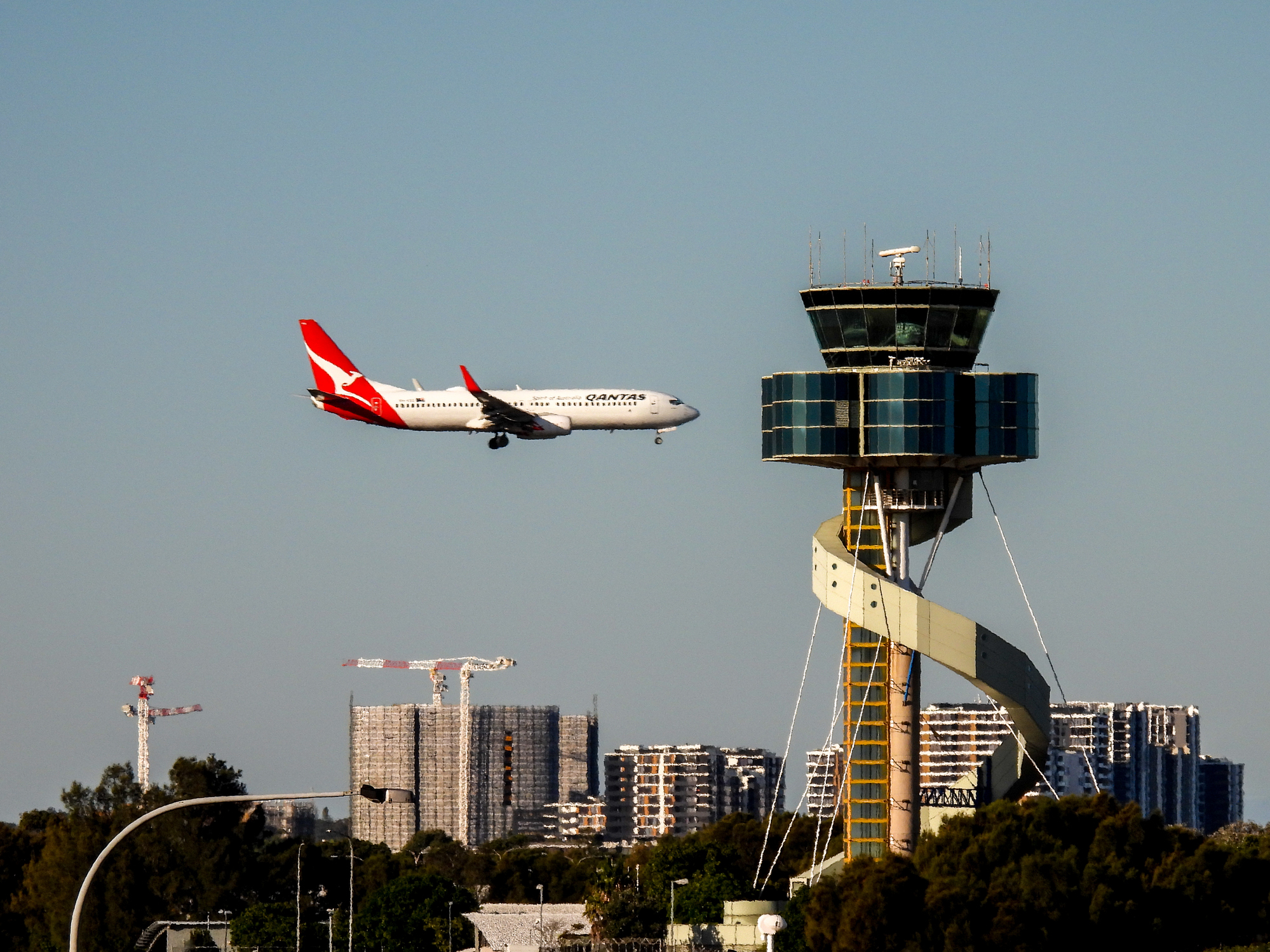Et Qantas-fly nærmer sig Sydney Lufthavn med det markante lufthavnstårn længere tilbage.