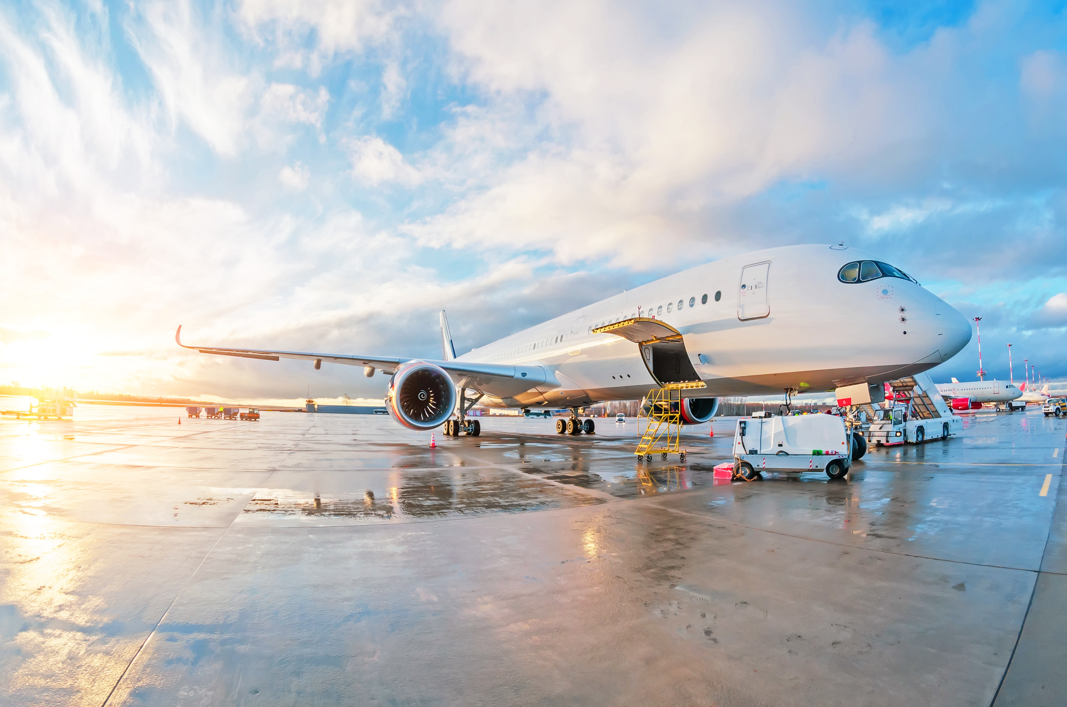 Vedligeholdelsesarbejde på et parkeret passagerfly på vådt underlag i lufthavnen ved solnedgang