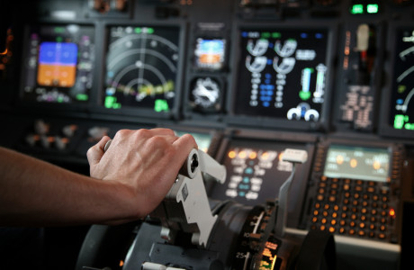 En hånd skubber en kontrol fremad, med adskillige målere og målere i et cockpit i baggrunden.