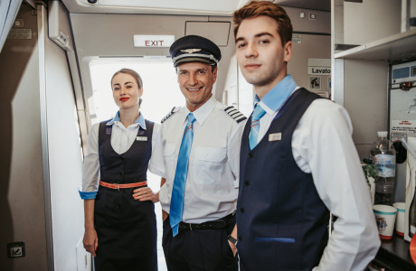 Piloten og to stewardesser hilser smilende på passagererne.
