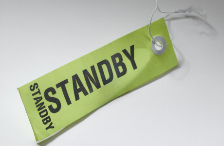 Et taskeetiket med påskriften "STANDBY" ligger på en hvid overflade.