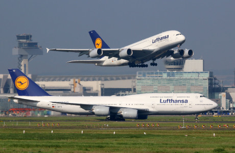 I forgrunden er et Lufthansa-fly på startbanen i en lufthavn, og i baggrunden er et andet fly lige ved at lette.