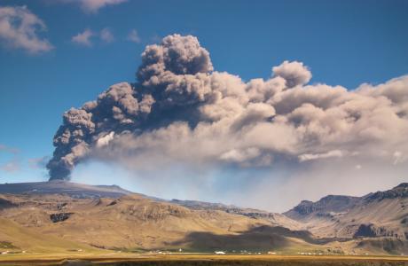 Nogle huse i Island kan ses i forgrunden med Eyjafjallajökull og dens askesky i baggrunden.