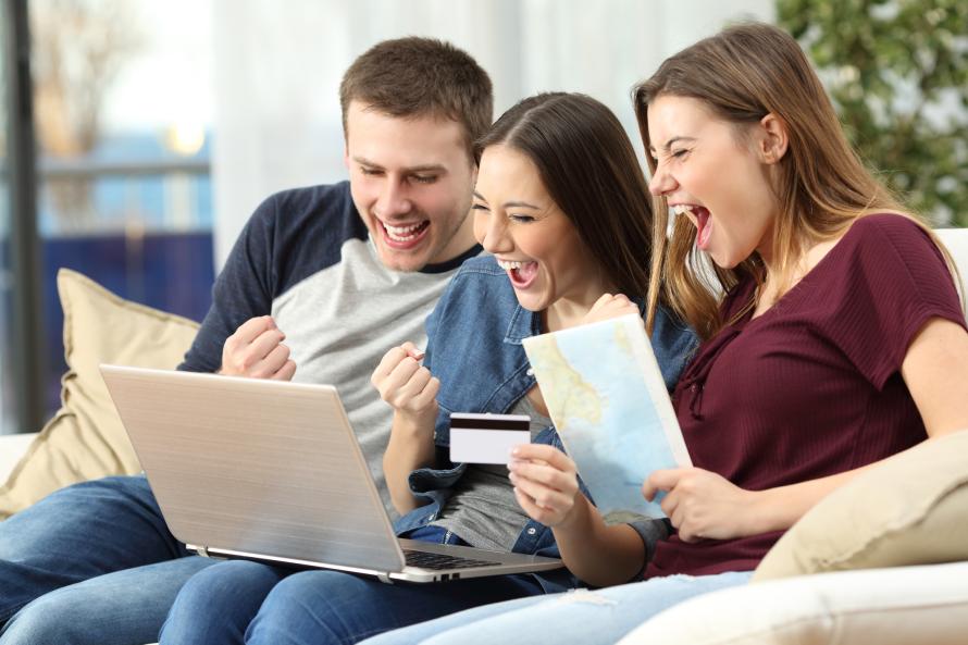 Tre unge personer sidder jublende foran en bærbar computer.